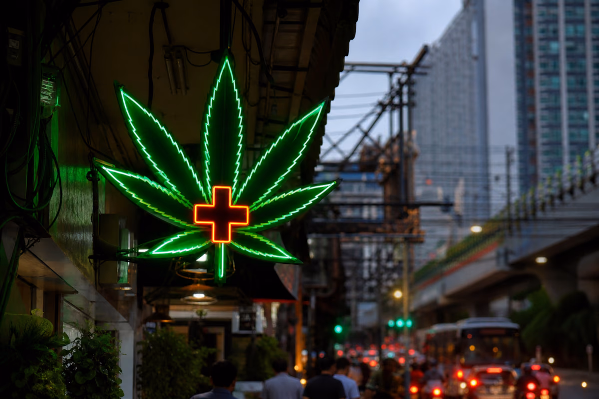 Neon cannabis leaf sign with medical cross above a busy Bangkok street with BTS Skytrain in background